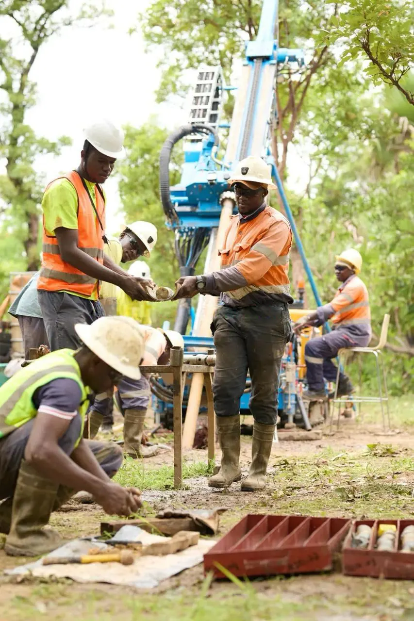 Two geologists passing a fresh drill core sample in front of the rig at Komassala Sud
